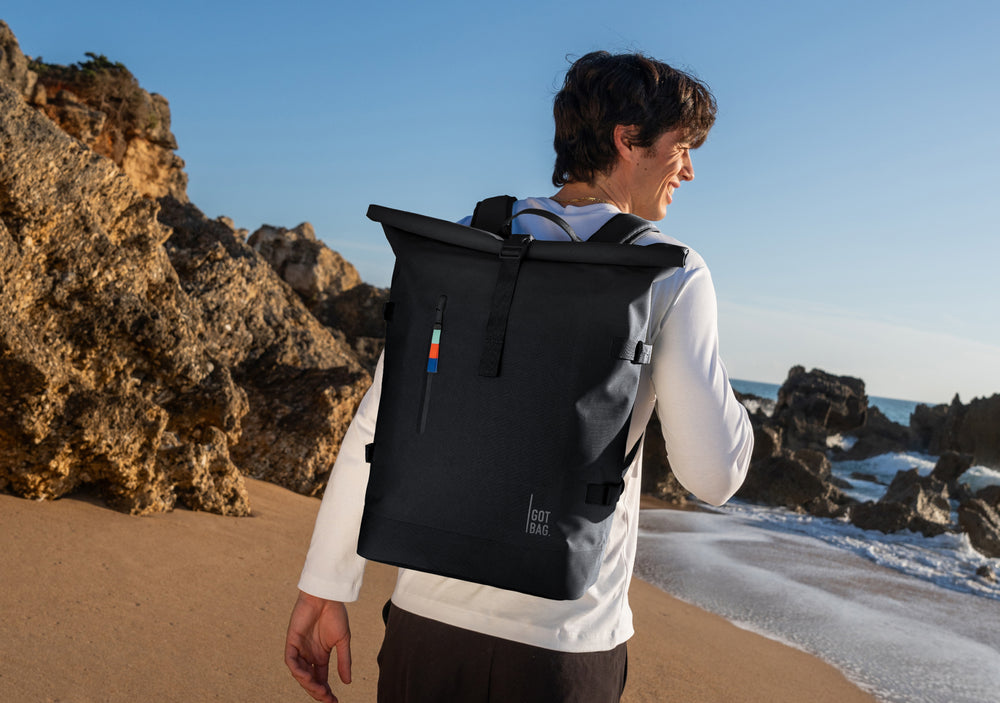 ROLLTOP backpack in black (classic black) carried as a backpack by a man on his back.