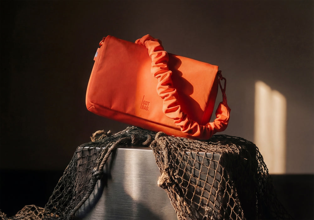 LUCID BAG bag in hot coral (vibrant orange) with ruffled strap on dark background.