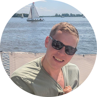 Accessories worn by a man who smiles outdoors with sunglasses in front of sailboats.