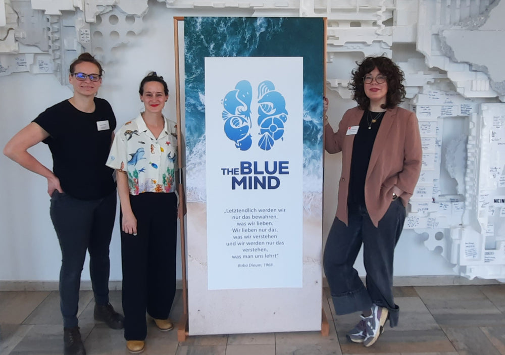 Tre donne sono davanti a un accessorio banner THE BLUE MIND, che mostra un cervello di motivi marini.