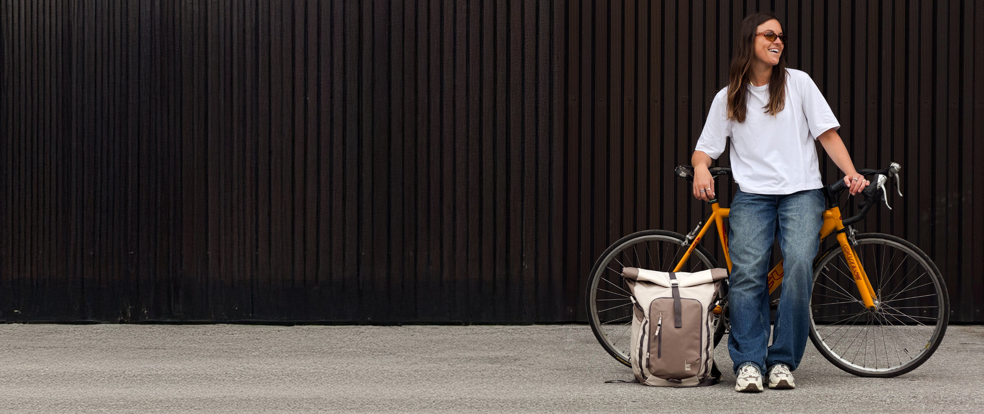 Rucksack am Boden neben einem gelben Fahrrad, daneben steht eine Frau.