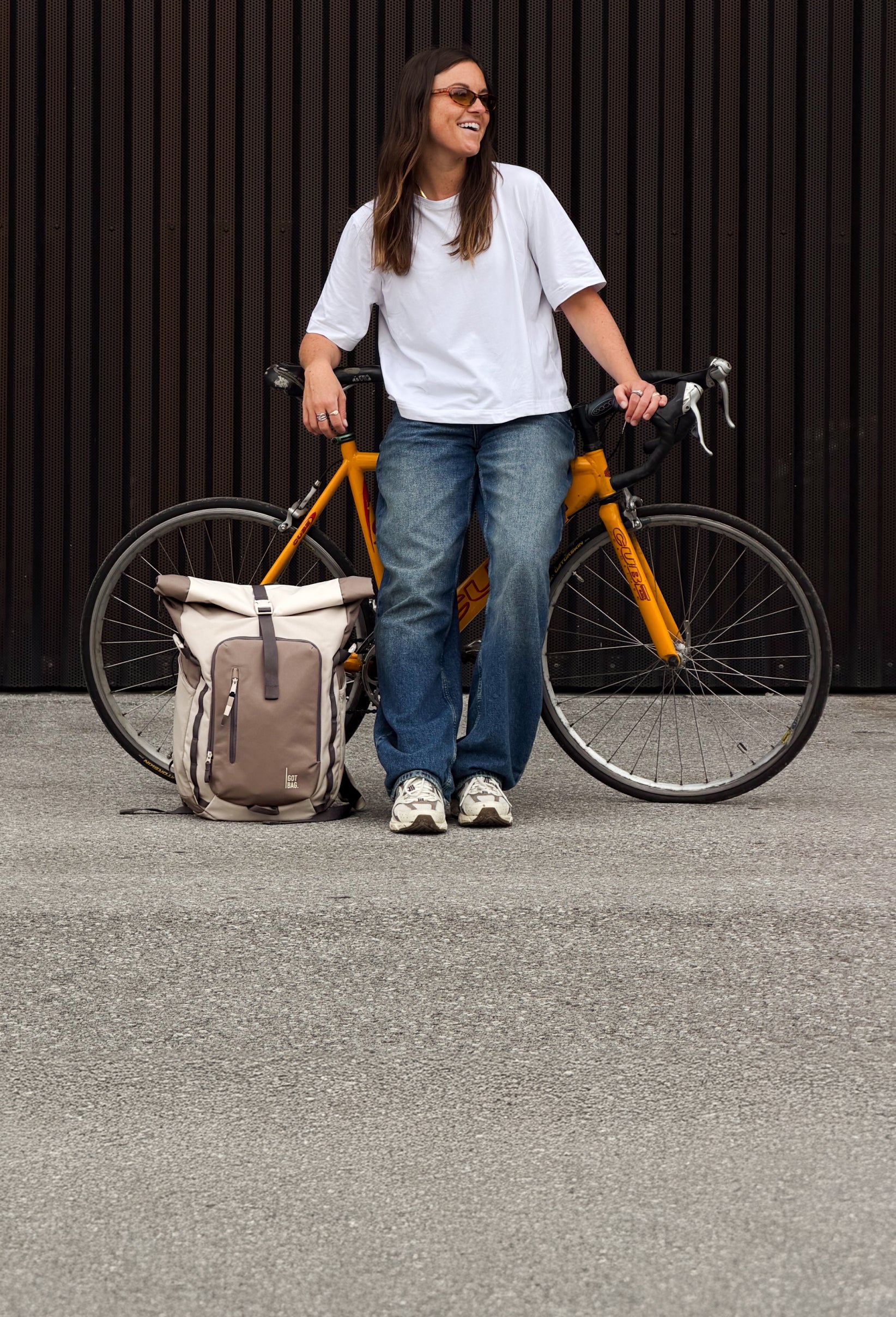 Rucksack am Boden neben einem gelben Fahrrad, daneben steht eine Frau.