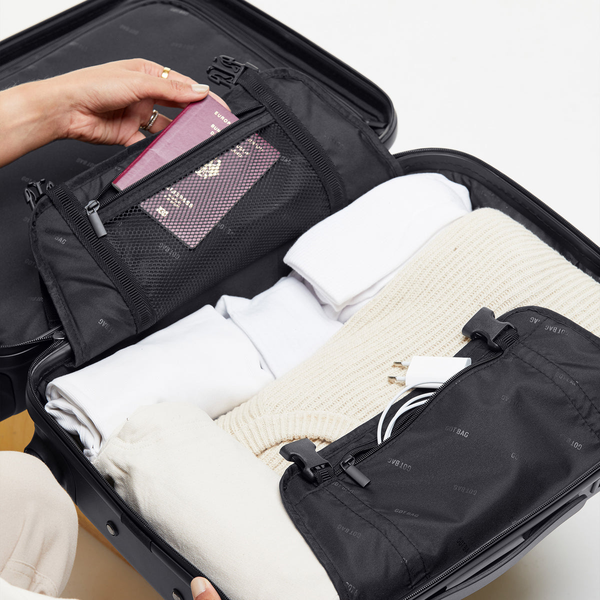 RE-SHELL Cabin Koffer in black (Schwarz) von einer Person gepackt, ein Reisepass wird in eine Netztasche gelegt.