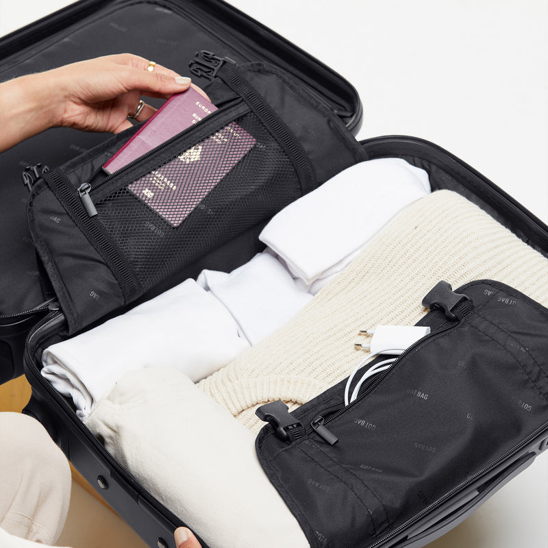 RE-SHELL Cabin Koffer in black (Schwarz) von einer Person gepackt, ein Reisepass wird in eine Netztasche gelegt.