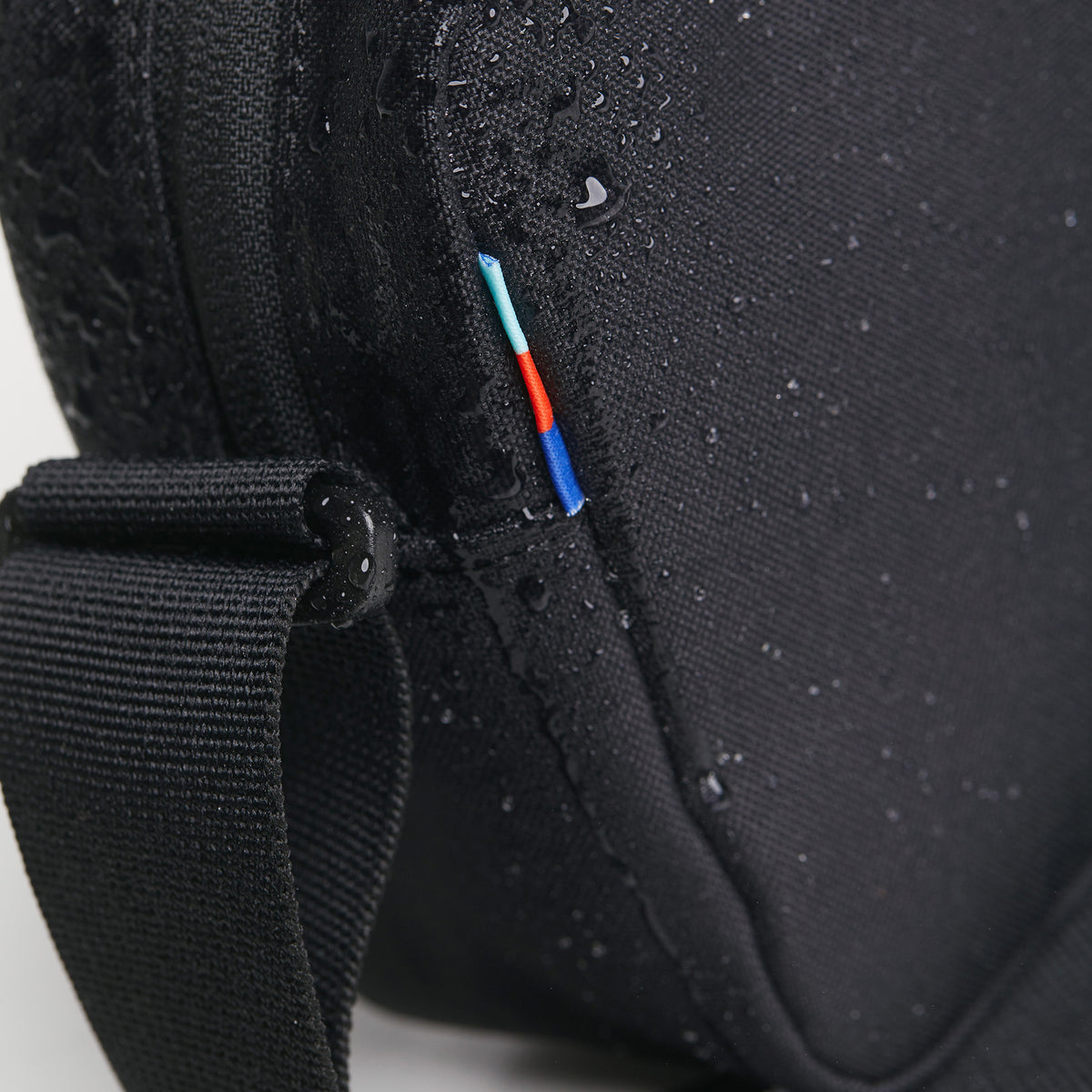 CROSSBODY Tasche in black (Schwarz) als Detailaufnahme mit Wassertropfen und farbigem Detail.