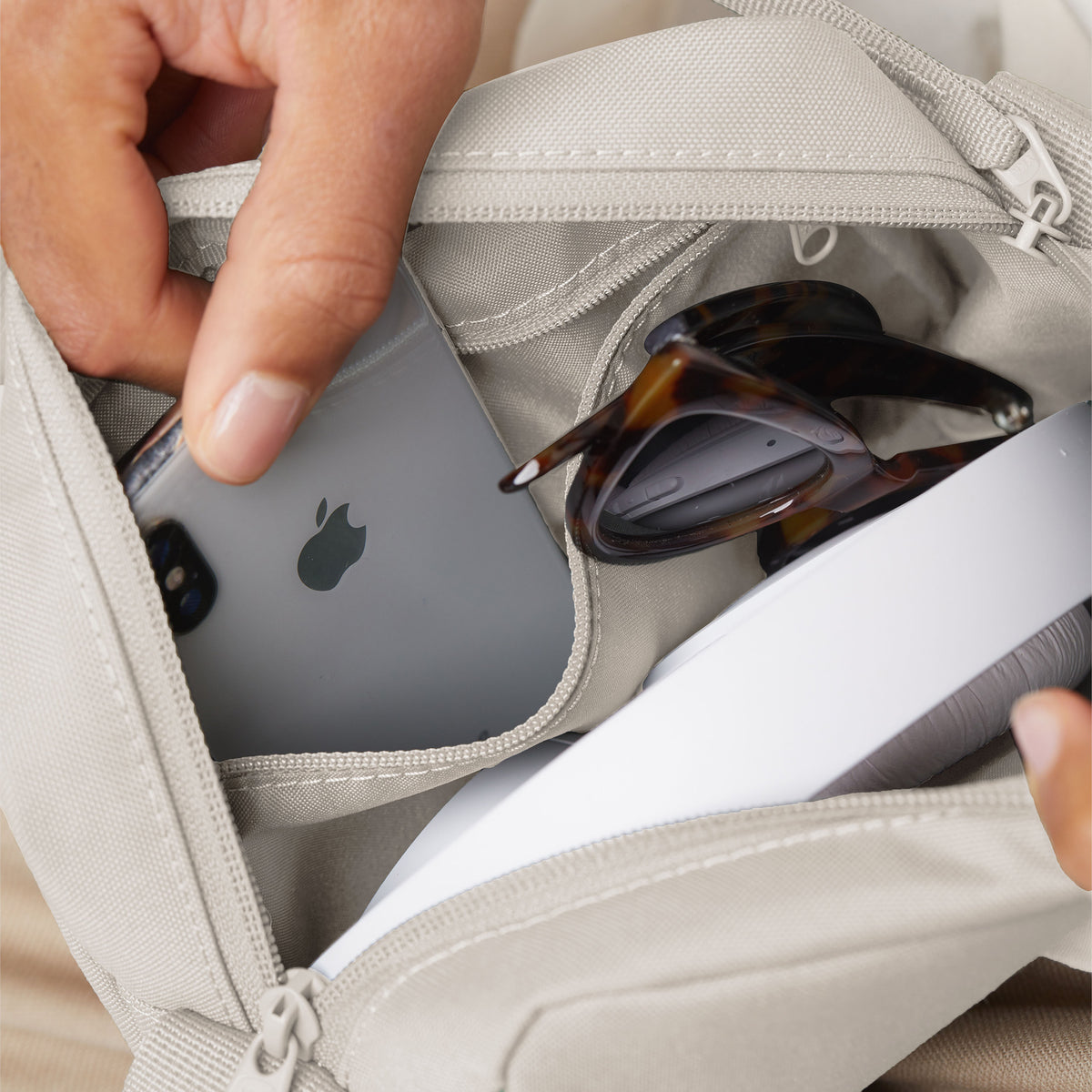 CROSSBODY Tasche in soft shell (warmes Cremeweiß), eine Hand legt ein Smartphone in eine Innentasche.
