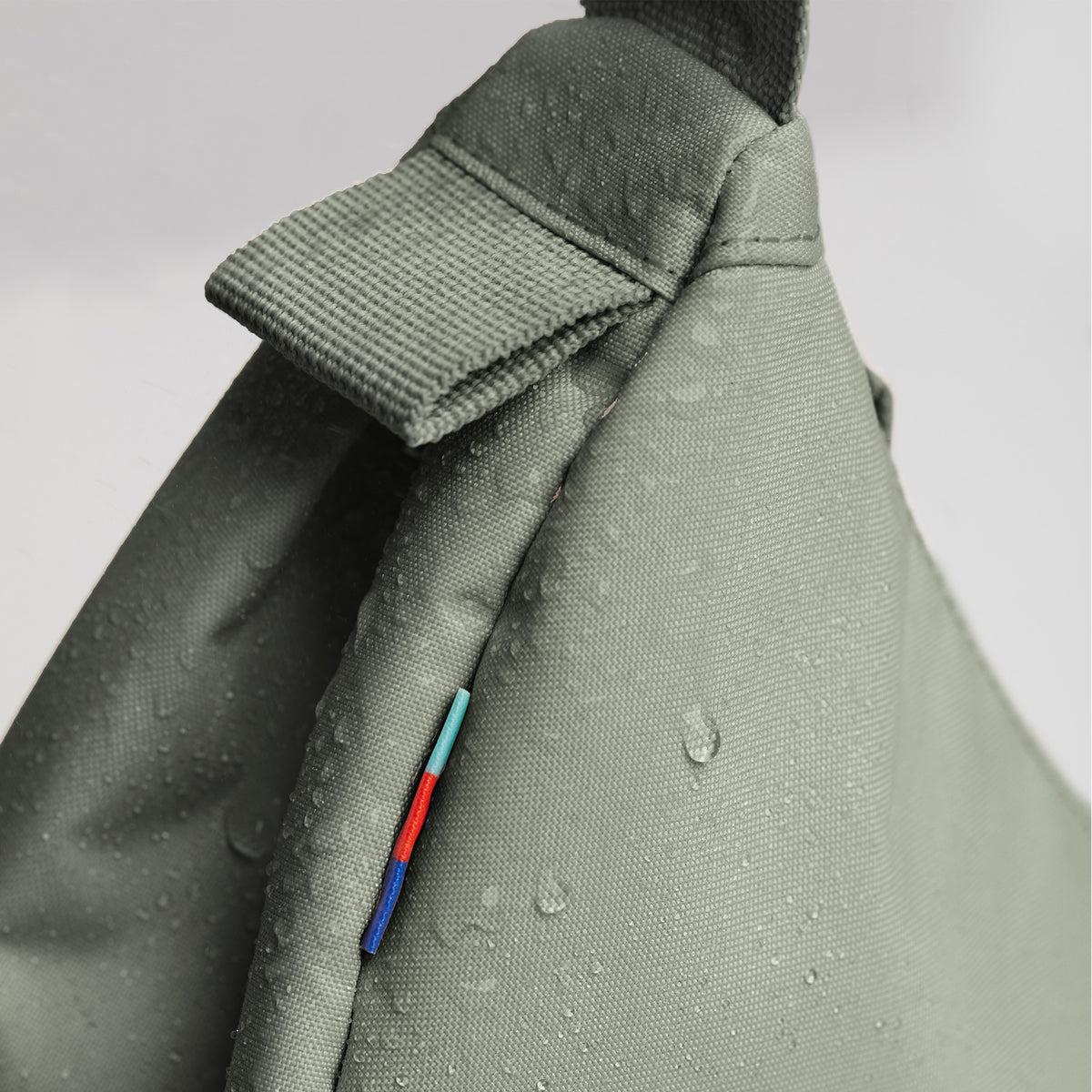 MOON BAG SMALL Tasche in bass (Salbeigrün) als Detailaufnahme mit Wassertropfen und bunten Streifen.