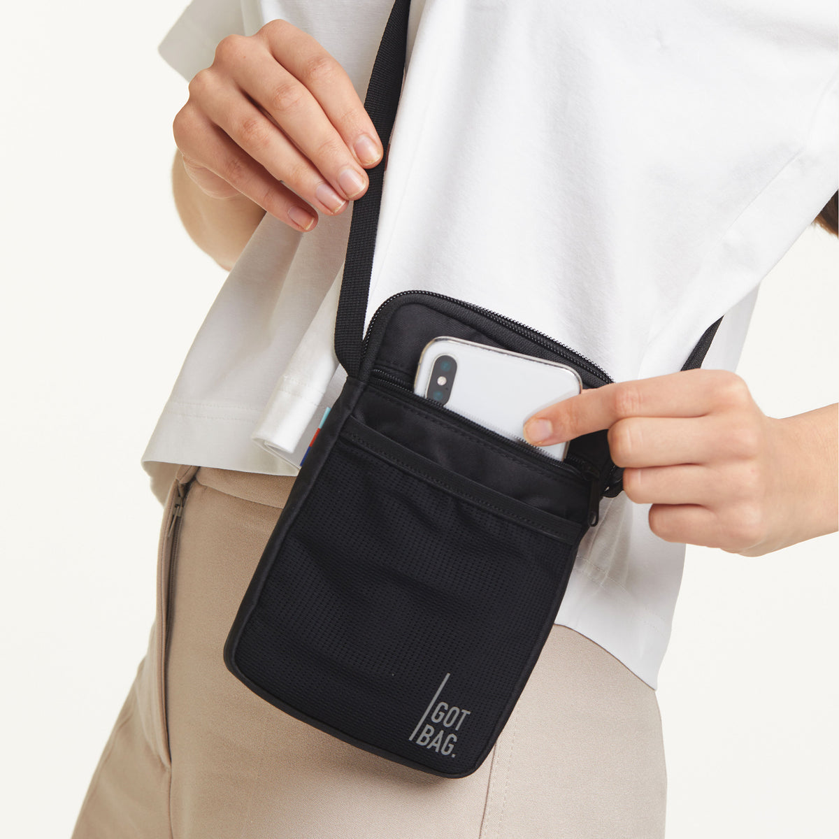 NANO BAG Tasche in black (Schwarz) von einer Frau crossbody getragen, die ein Smartphone verstaut.