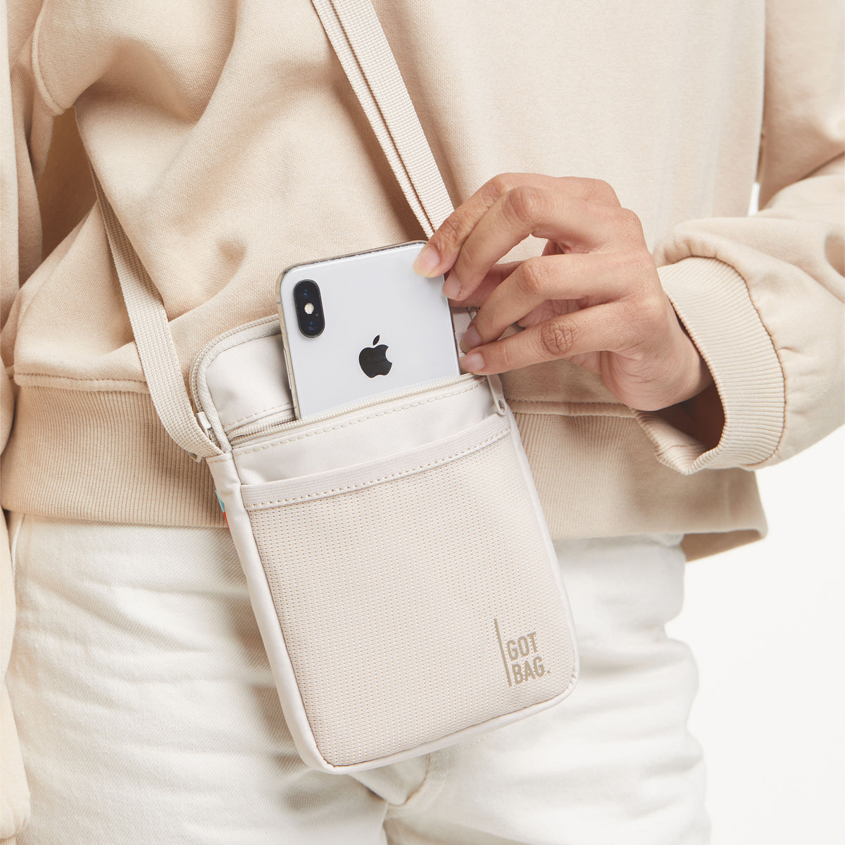 NANO BAG Tasche in soft shell (warmes Cremeweiß), crossbody getragen, eine Hand steckt ein Handy hinein.