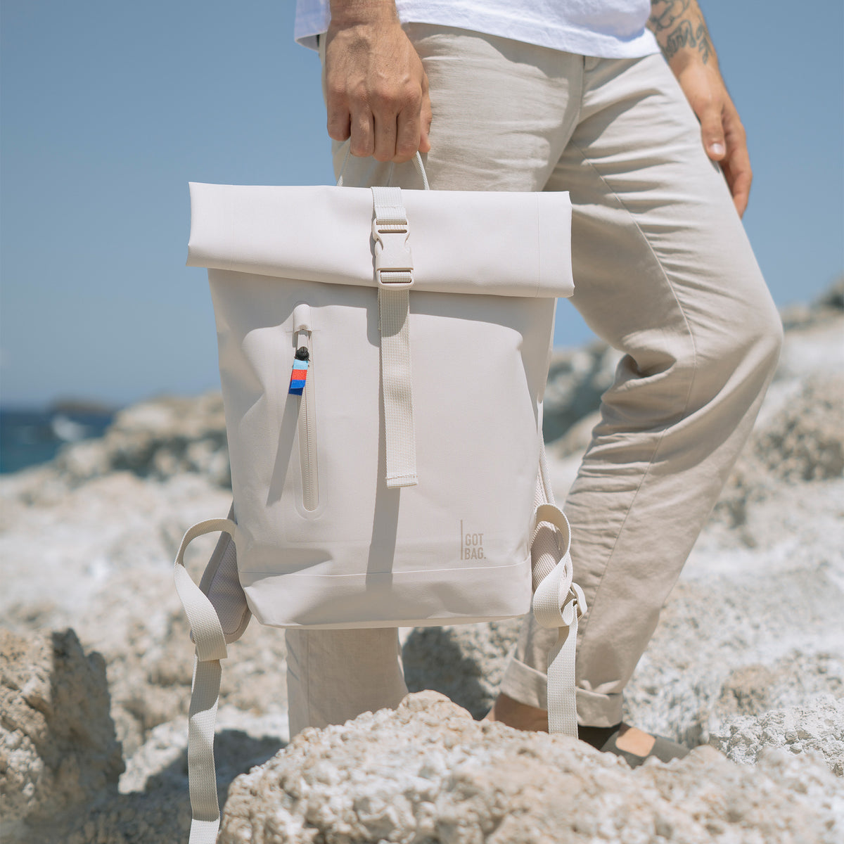 ROLLTOP SMALL Rucksack in soft shell (warmes Cremeweiß) von einem Mann in der Hand gehalten.