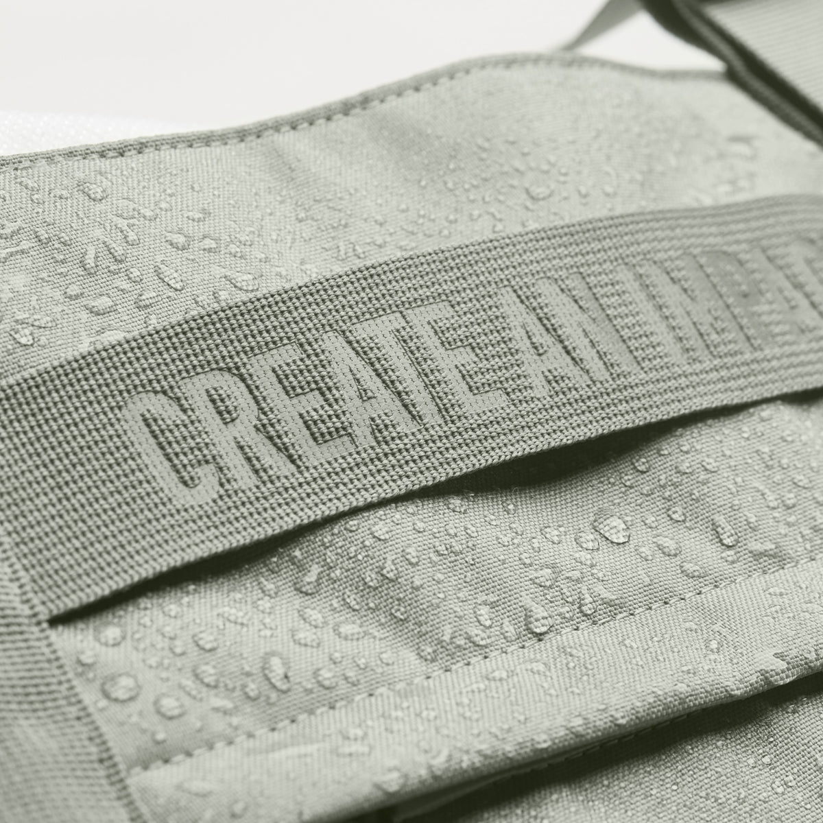 TOTE BAG Tasche in bass (Salbeigrün), Detailaufnahme des wasserabweisenden Stoffes mit Wassertropfen und Textilband.
