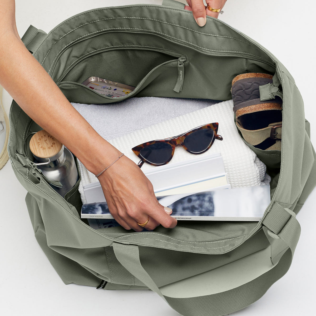 TOTE BAG Tasche in bass (Salbeigrün), in die eine Frau greift.
