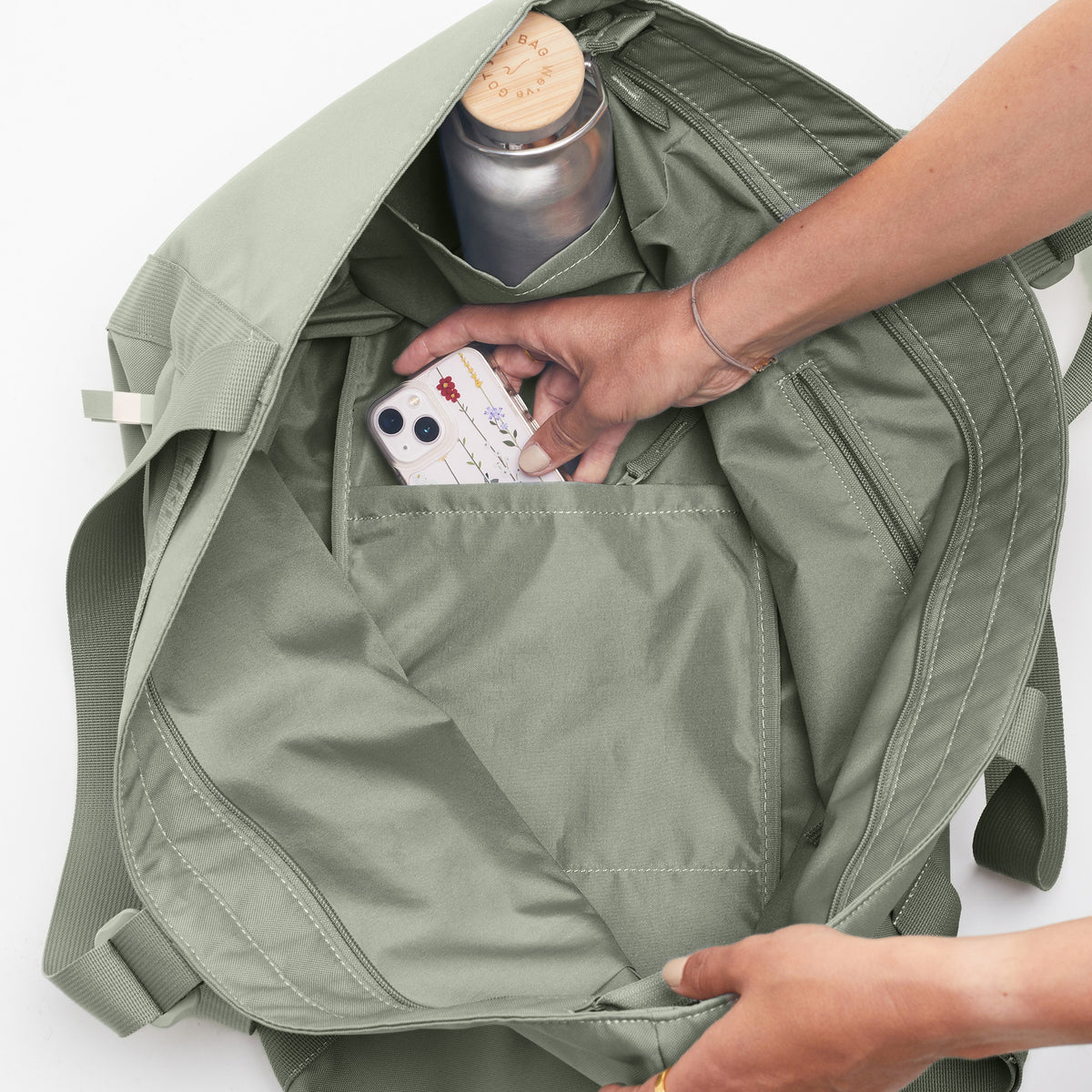 TOTE BAG Tasche in bass (Salbeigrün), die von einer Frau mit einem Handy befüllt wird.