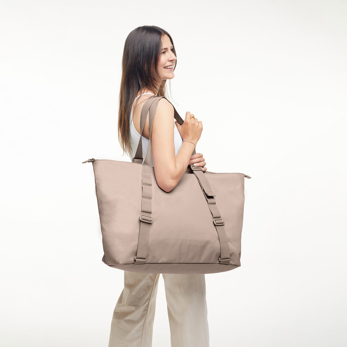 TOTE BAG Monochrome Edition Tasche in seal (dunkler Beigeton) von einer Frau über der Schulter getragen.