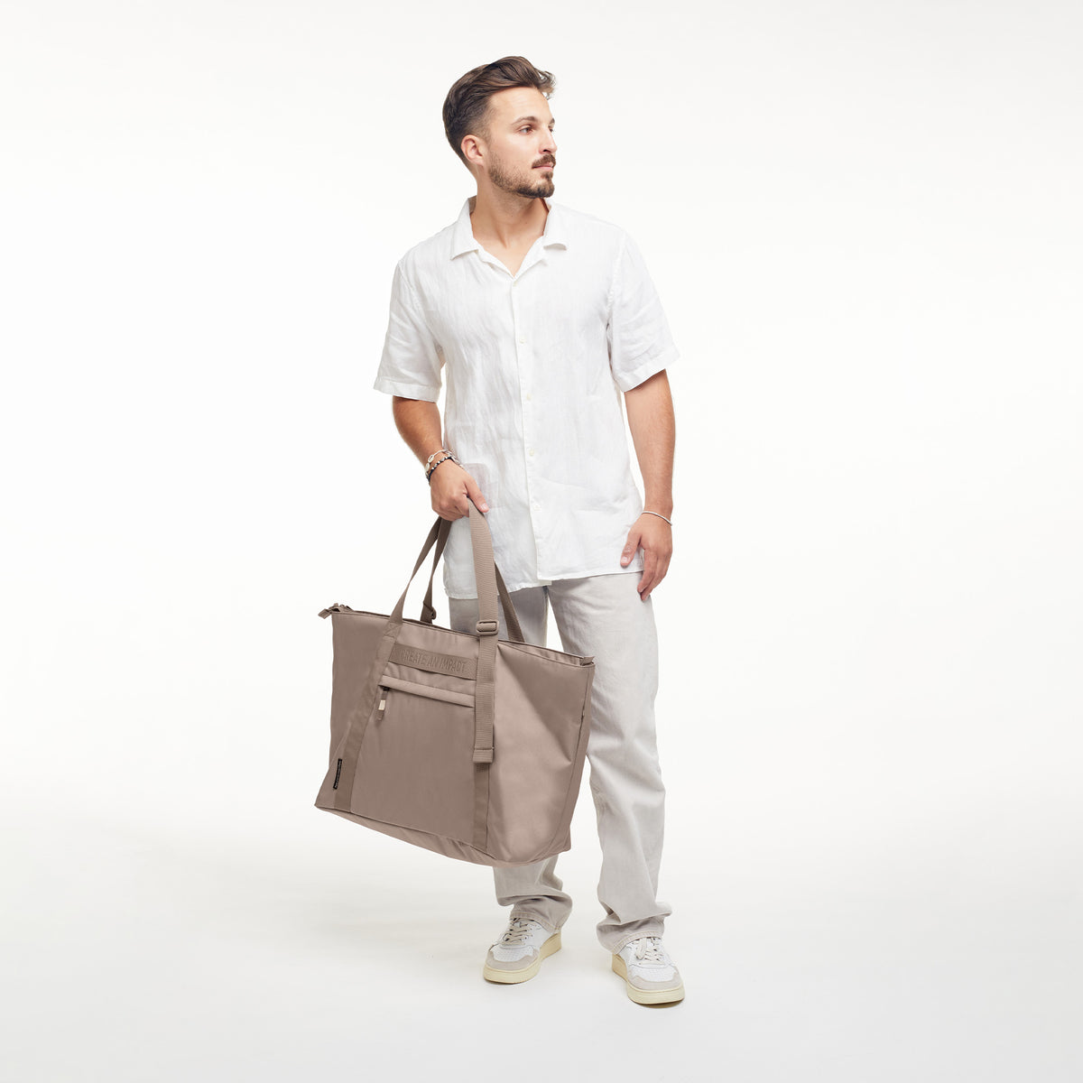 TOTE BAG Tasche in seal (dunkler Beigeton) von einem Mann in der Hand gehalten.