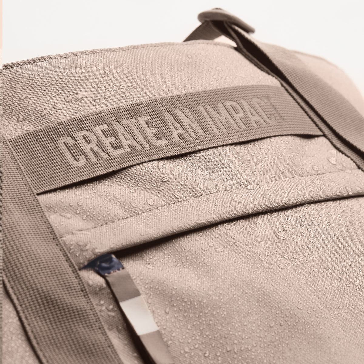 TOTE BAG Tasche in seal (dunkler Beigeton) Detailaufnahme mit Wassertropfen und Schriftzug CREATE AN IMPACT.