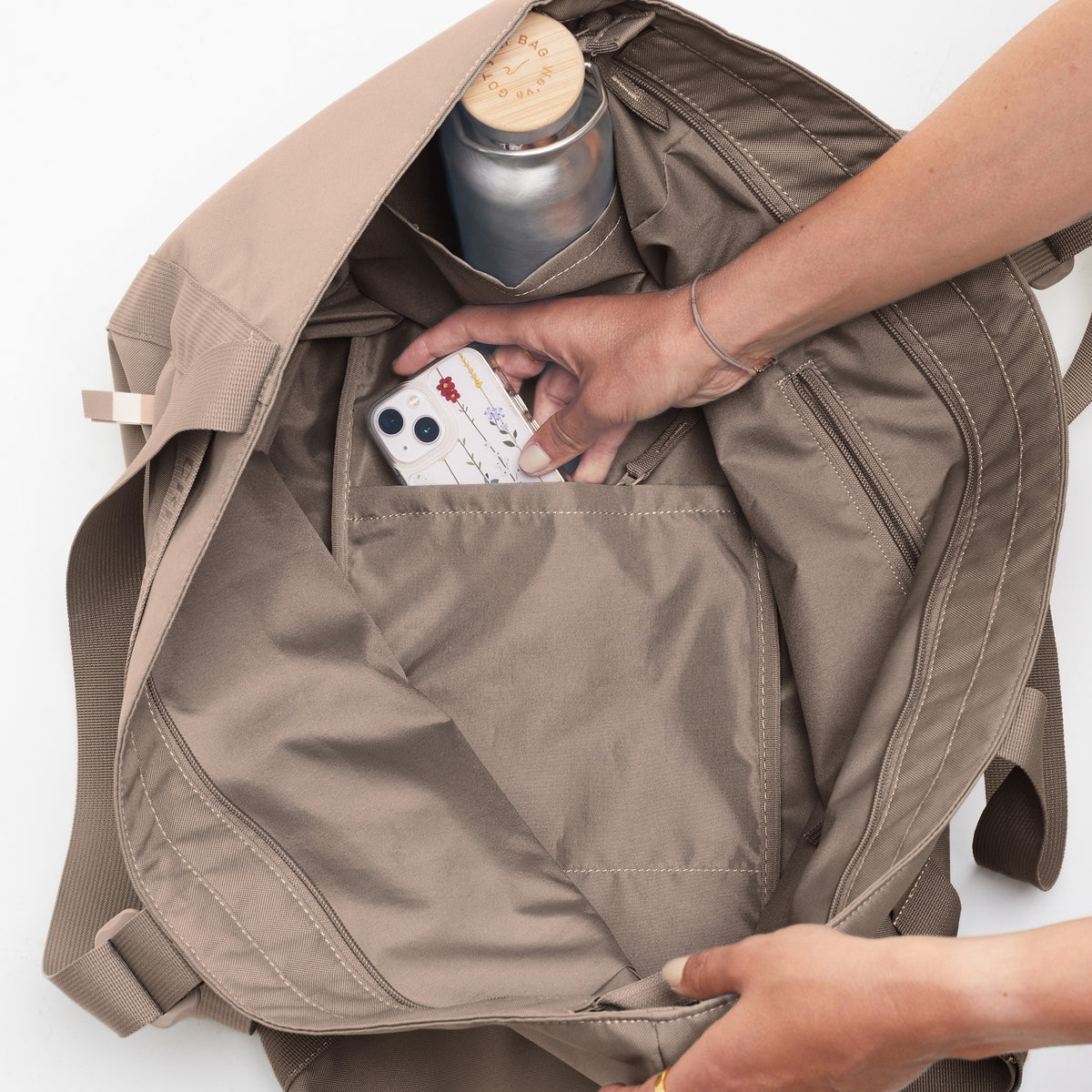 TOTE BAG Tasche in seal (dunkler Beigeton), eine Frau legt ein Handy in die Innentasche.