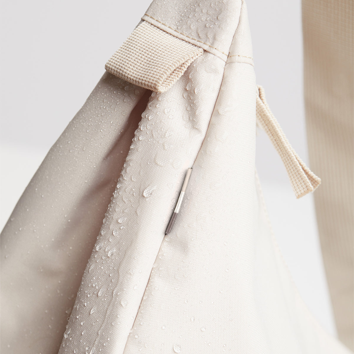 MOON BAG SMALL Tasche in soft shell (warmes Cremeweiß), Detailaufnahme mit Wassertropfen und Reißverschluss.