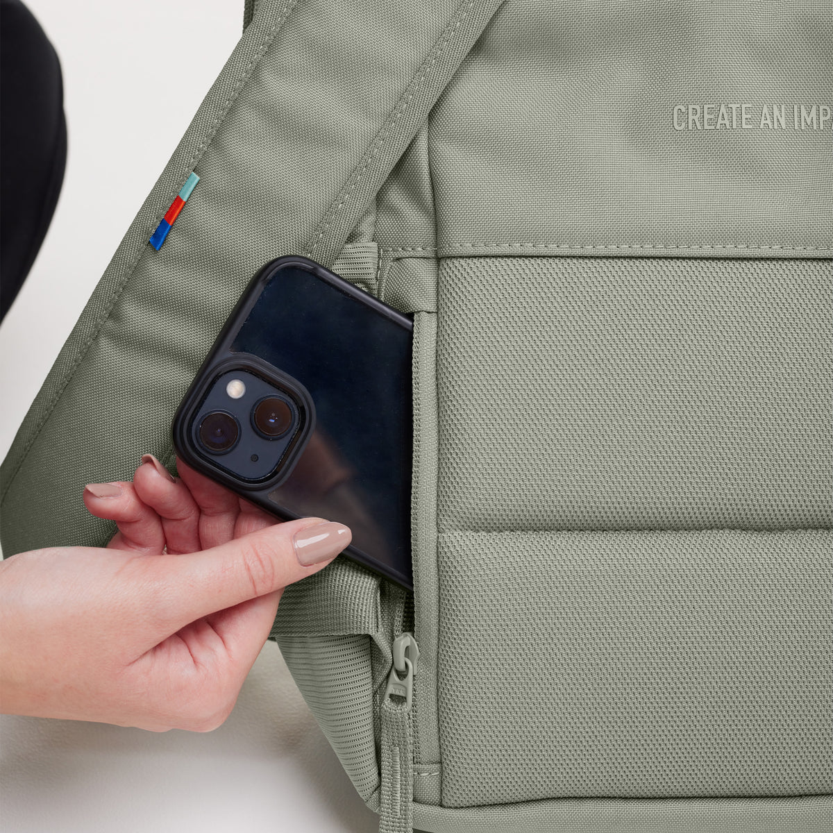 DAYPACK 2.0 Rucksack in bass (Salbeigrün). Eine Frau entnimmt ein Handy aus der Tasche.