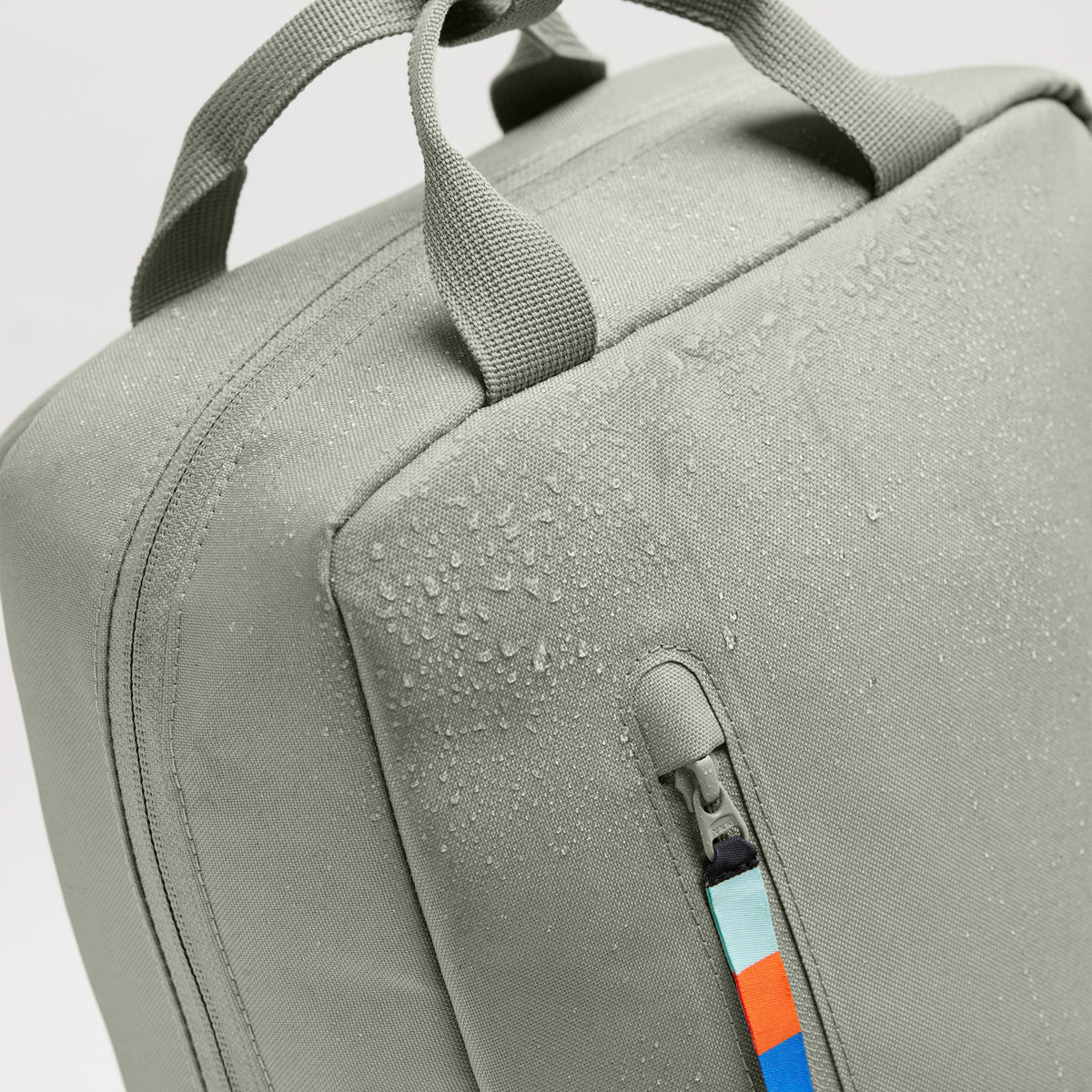 DAYPACK Rucksack in bass (Salbeigrün) als Detailaufnahme des wasserabweisenden Stoffs mit Wassertropfen und Reißverschluss.