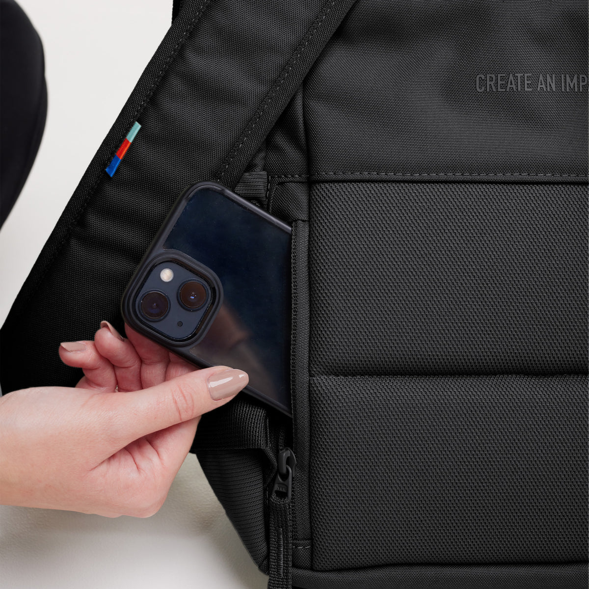DAYPACK Rucksack in black (Schwarz). Detailaufnahme einer Frau, die ein Smartphone aus der Seitentasche nimmt.