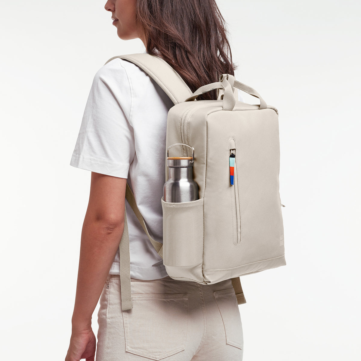 DAYPACK 2.0 Rucksack in soft shell (warmes Cremeweiß) von einer Frau auf dem Rücken getragen, Trinkflasche in Seitentasche.