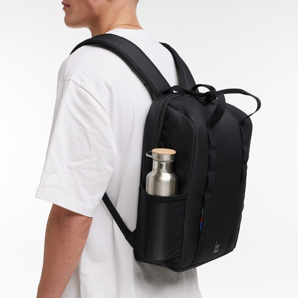DAYPACK LOOP Rucksack in black (Schwarz), von einem Mann auf dem Rücken getragen, mit Trinkflasche in Netztasche.