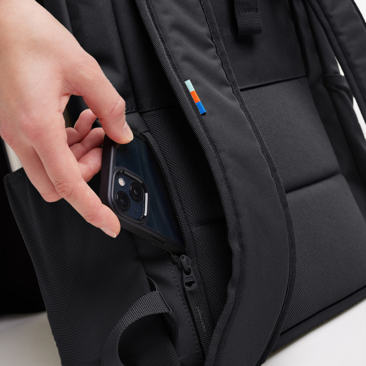 DAYPACK LOOP Rucksack in black (Schwarz). Eine Hand entnimmt ein Telefon aus einer Reißverschlusstasche.