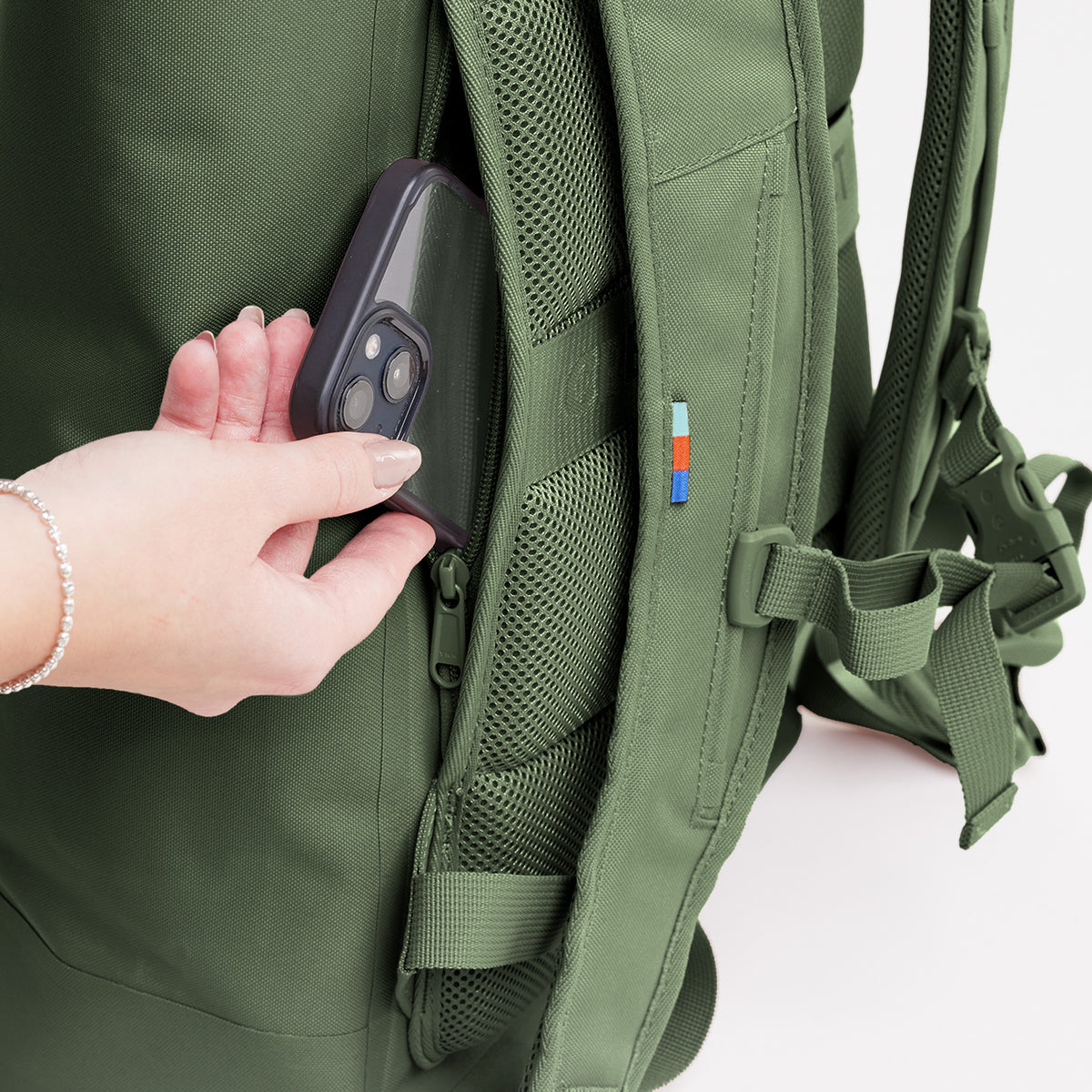 ROLLTOP LITE Rucksack in algae (Dunkelgrün mit Graustich), Detailaufnahme einer Frau, die ein Handy in die Seitentasche steckt.