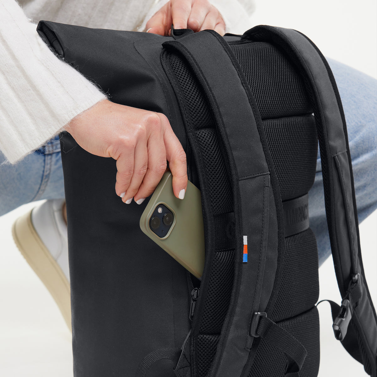 Frau steckt ein Smartphone in die Seitentasche eines ROLLTOP LITE Rucksacks.