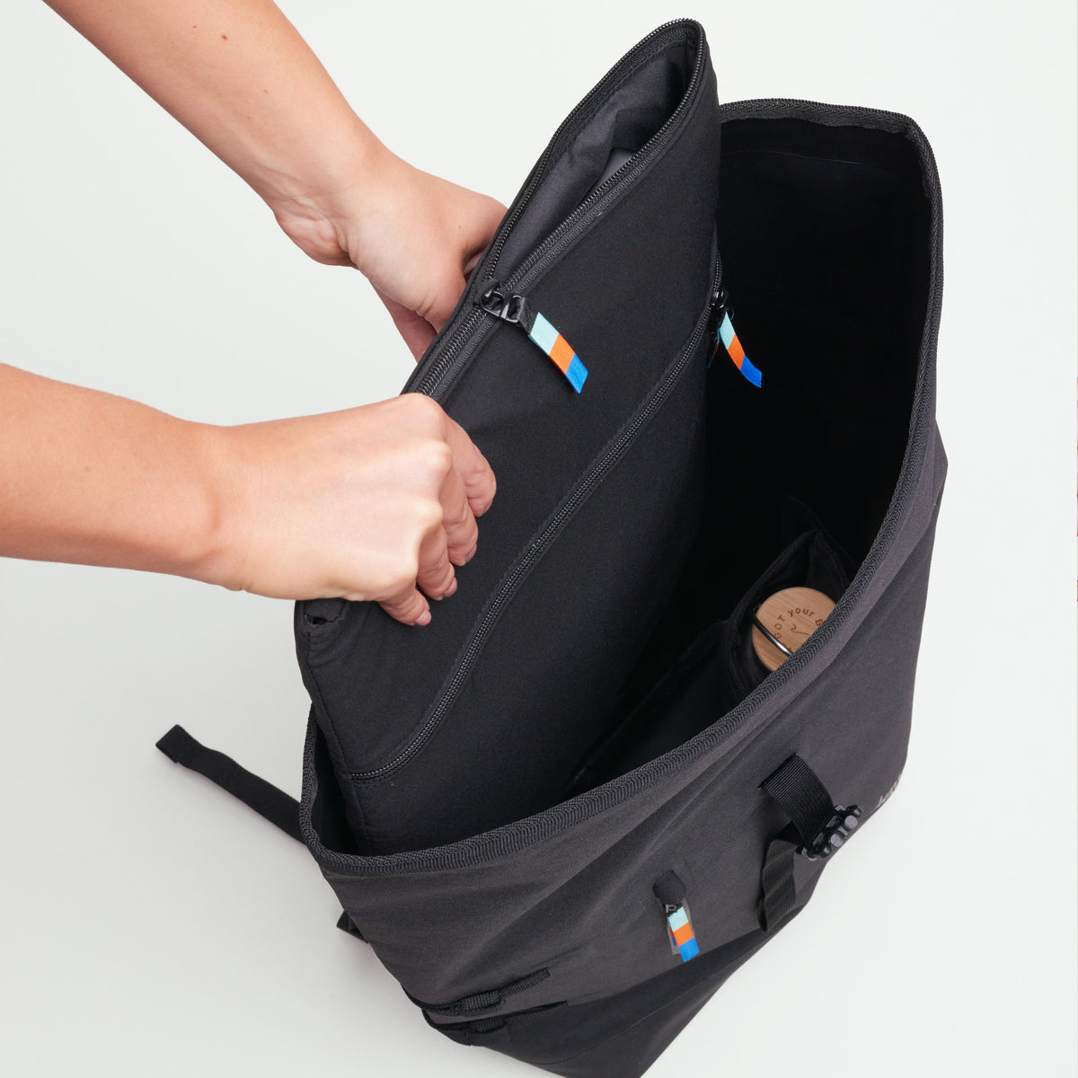 Eine Frau öffnet den ROLLTOP 2.0 Rucksack in black (Schwarz) und zeigt das Innenfach.