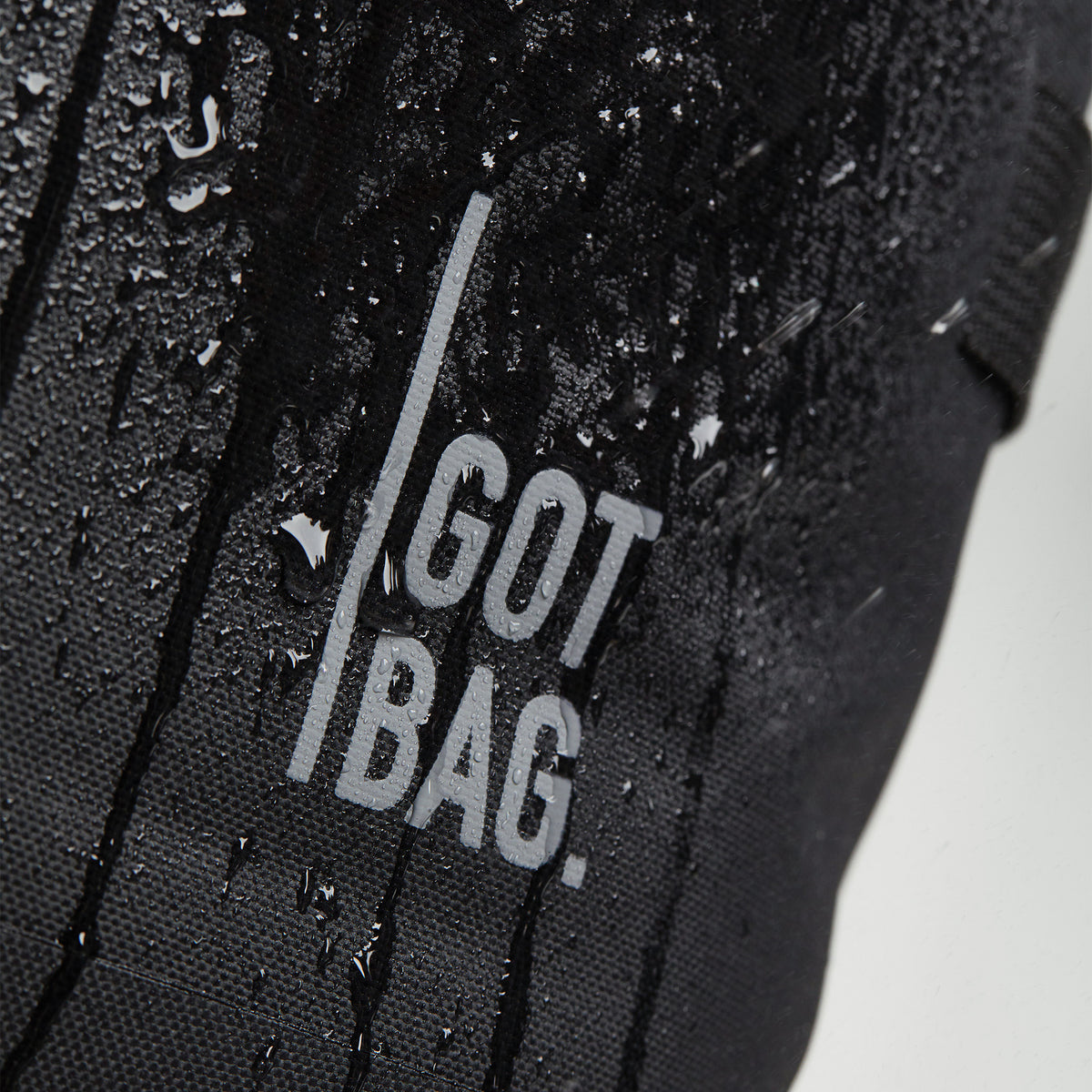 ROLLTOP 2.0 Rucksack in black (Schwarz) als Detailaufnahme mit Wassertropfen auf dem Material und Logo.