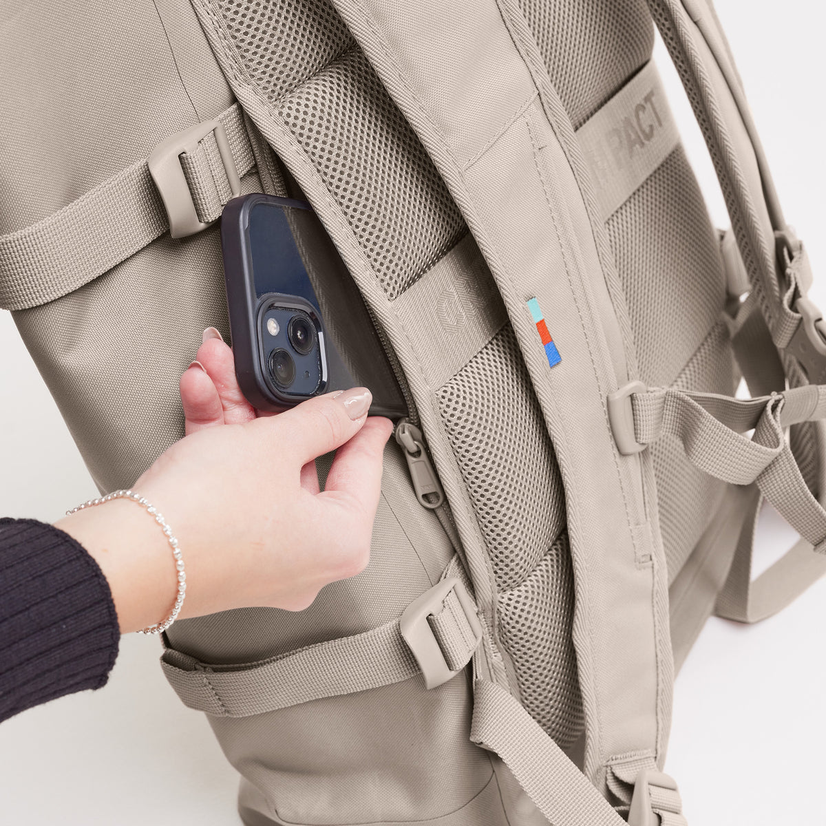 ROLLTOP 2.0 Rucksack in scallop (helles Beige) von einer Frau, die ein Handy in die Seitentasche steckt.