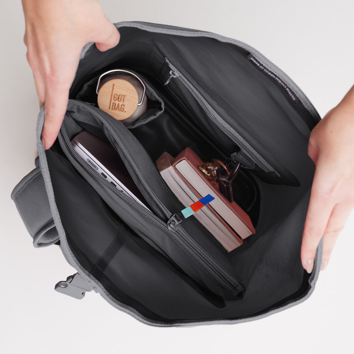 ROLLTOP 2.0 Rucksack in shark (Dunkelgrau), von Händen geöffnet, mit Laptop, Flasche und Büchern im Inneren.