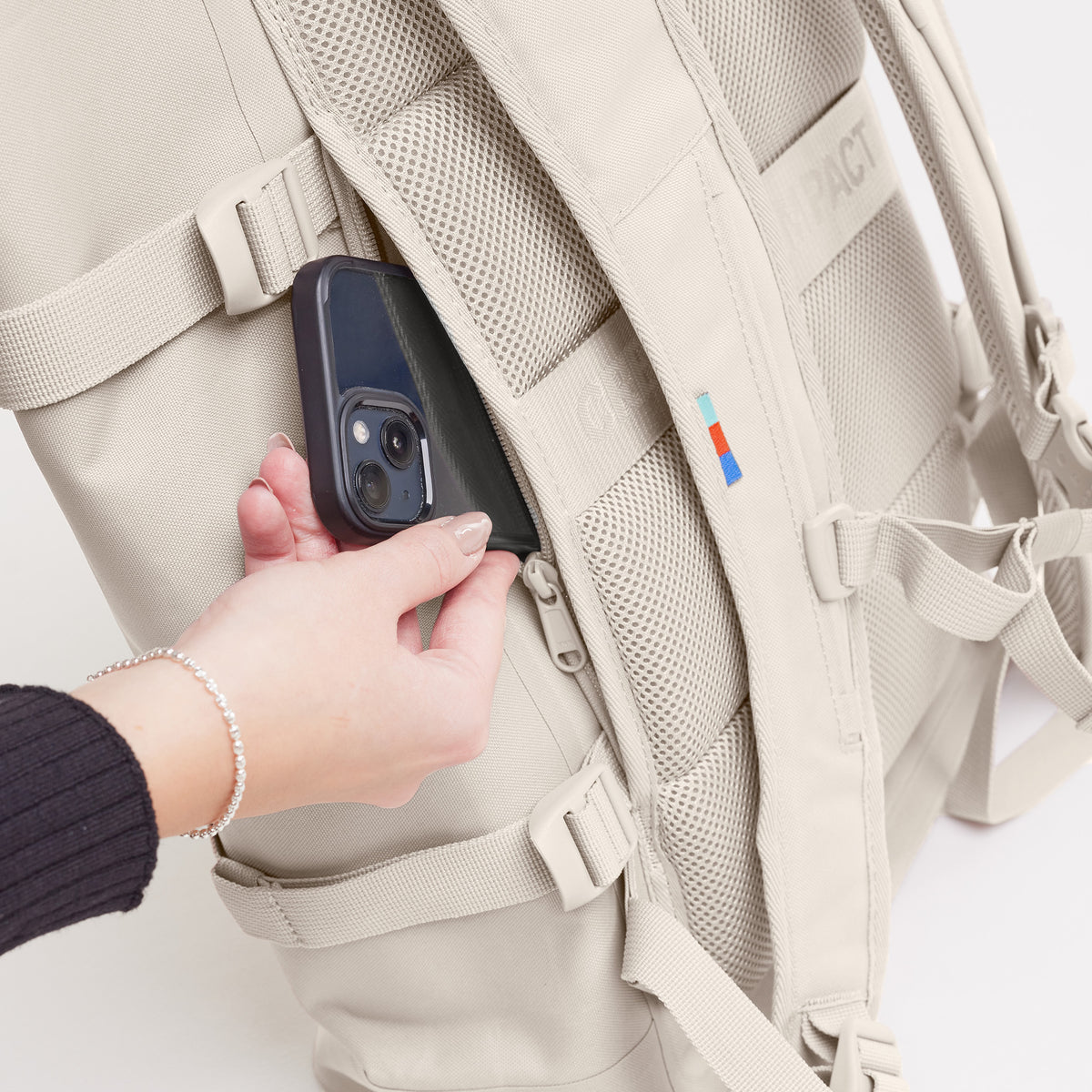 ROLLTOP Rucksack in soft shell (warmes Cremeweiß), Detailaufnahme einer Frau, die ein Handy in eine Reißverschlusstasche steckt.