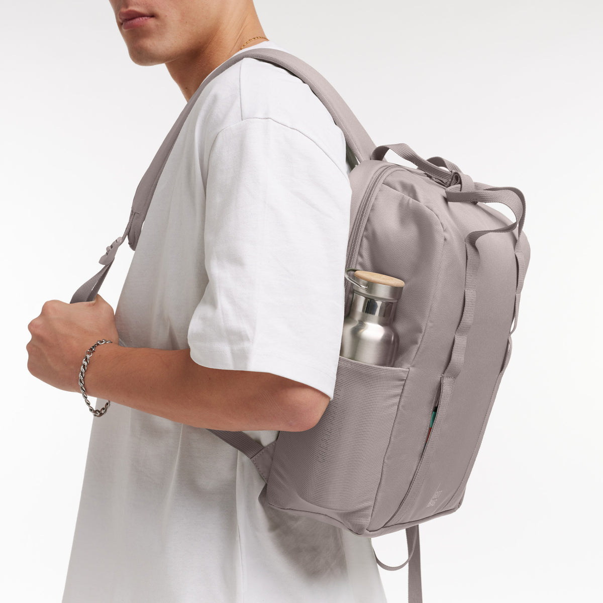 DAYPACK LOOP Rucksack in seahorse (graues Pastellrosa) von einem Mann auf dem Rücken getragen, mit Flasche im Seitenfach.