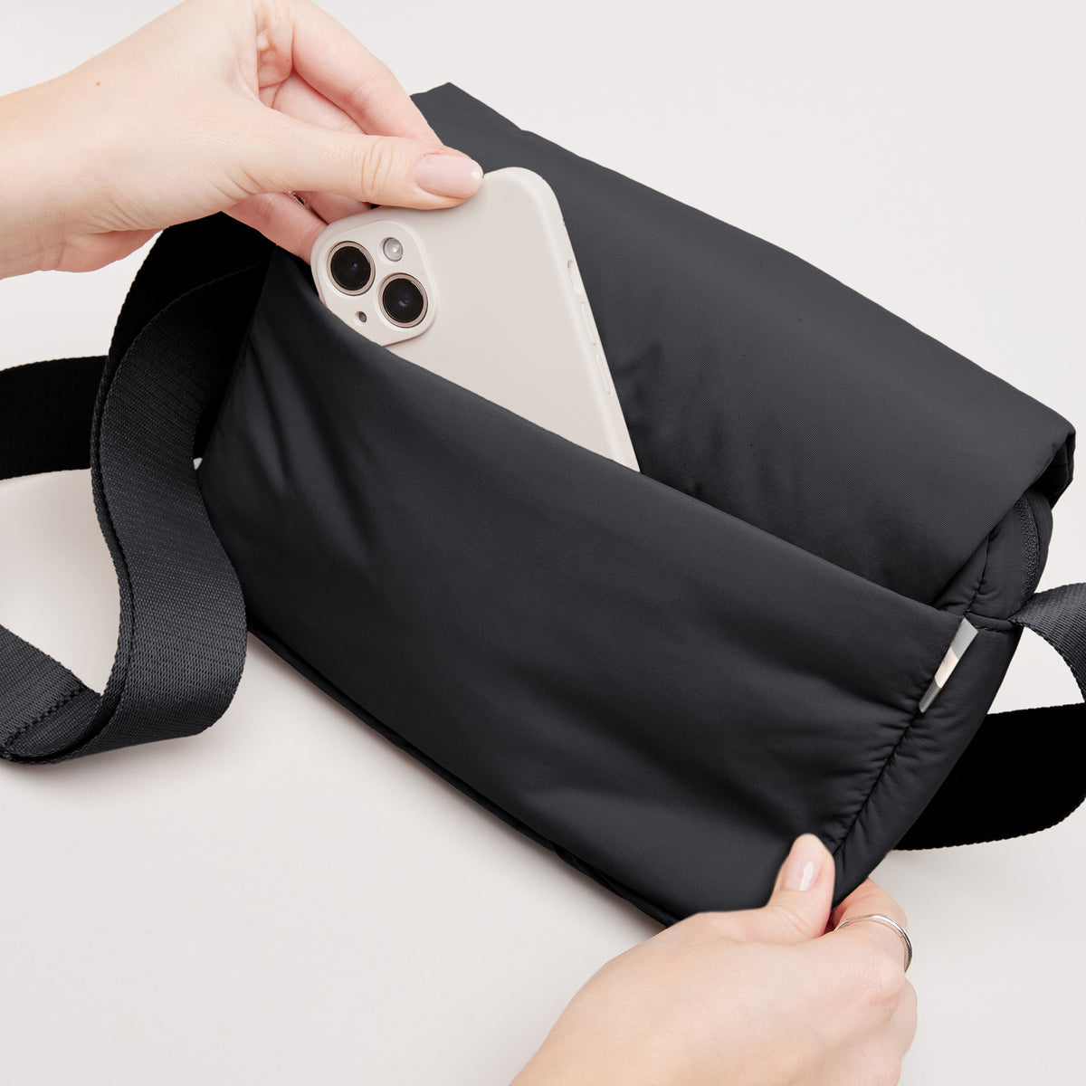 CLOUD CROSSBODY BAG Tasche in black (Schwarz), eine Frau legt ein Handy in die offene Tasche.