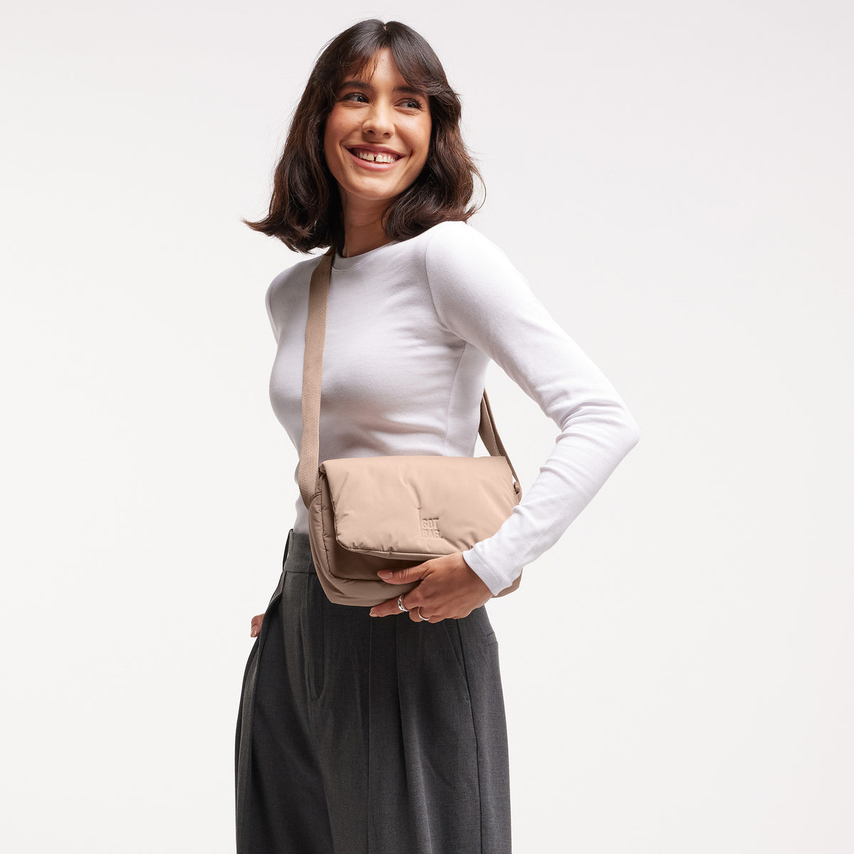 CLOUD CROSSBODY BAG Tasche in sandbar (warmes Beige mit rötlichem Unterton) von einer Frau crossbody getragen.