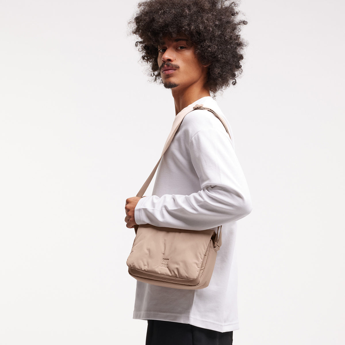 CLOUD CROSSBODY BAG Tasche in sandbar (warmes Beige mit rötlichem Unterton) von einem Mann crossbody getragen.