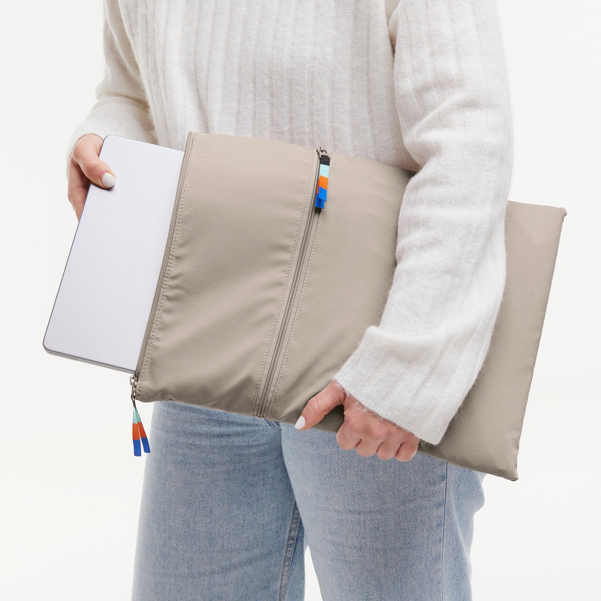 ROLLTOP LITE Tasche in scallop (helles Beige) von einer Frau gehalten, Laptop wird eingeschoben.