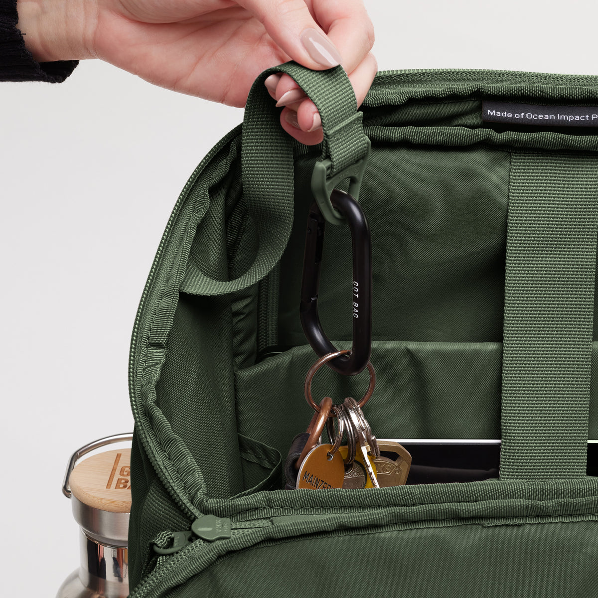 PRO PACK Rucksack in algae (Dunkelgrün mit Graustich), von einer Frau geöffnet, mit Karabiner und Schlüsseln innen.