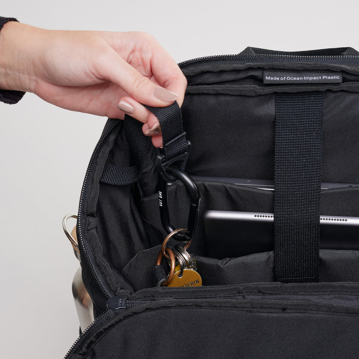 PRO PACK Rucksack in black (Schwarz), eine Frau befestigt Schlüssel mit Karabiner im Rucksack.