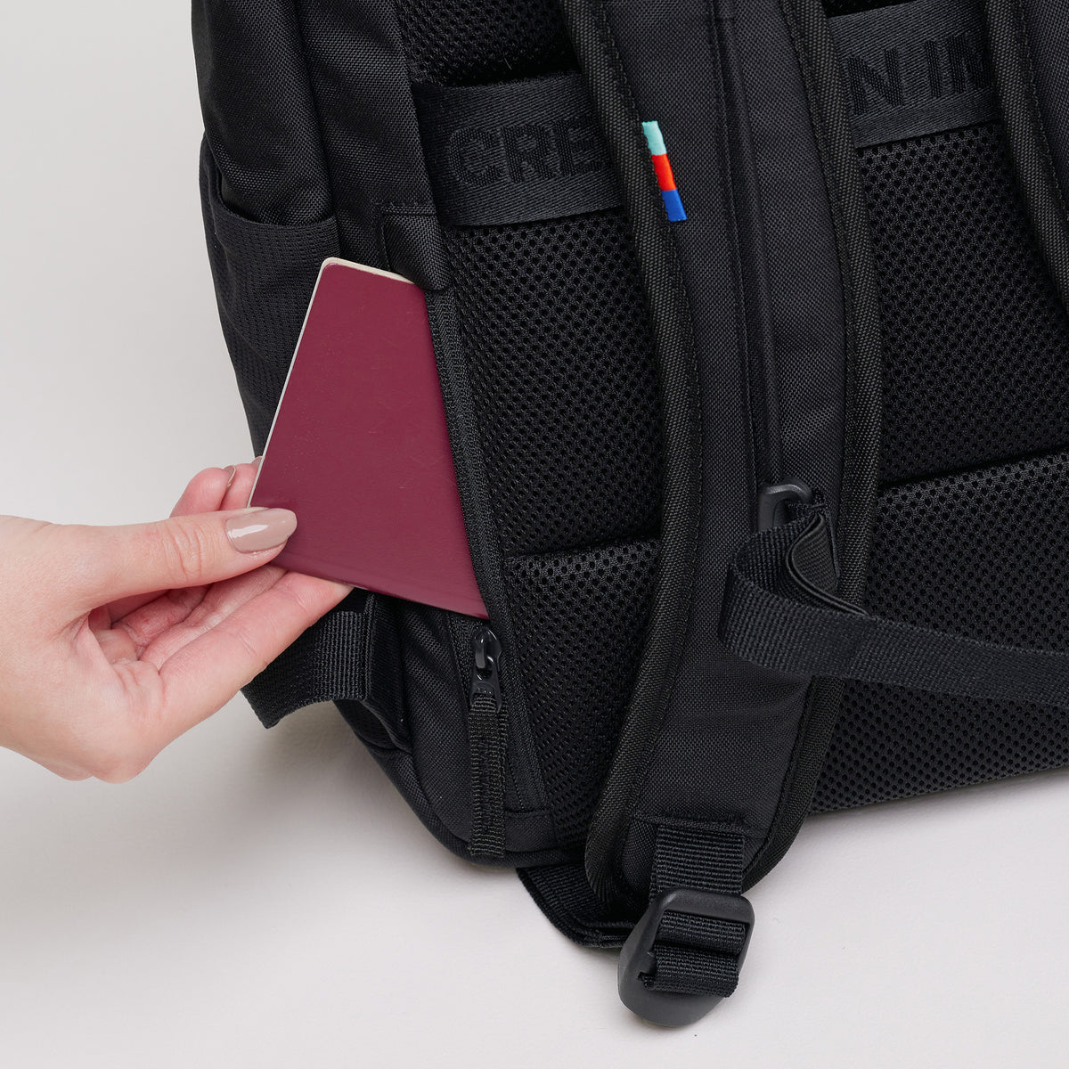 PRO PACK Rucksack in black (Schwarz), eine Hand steckt einen Pass in eine Tasche an der Rückseite.