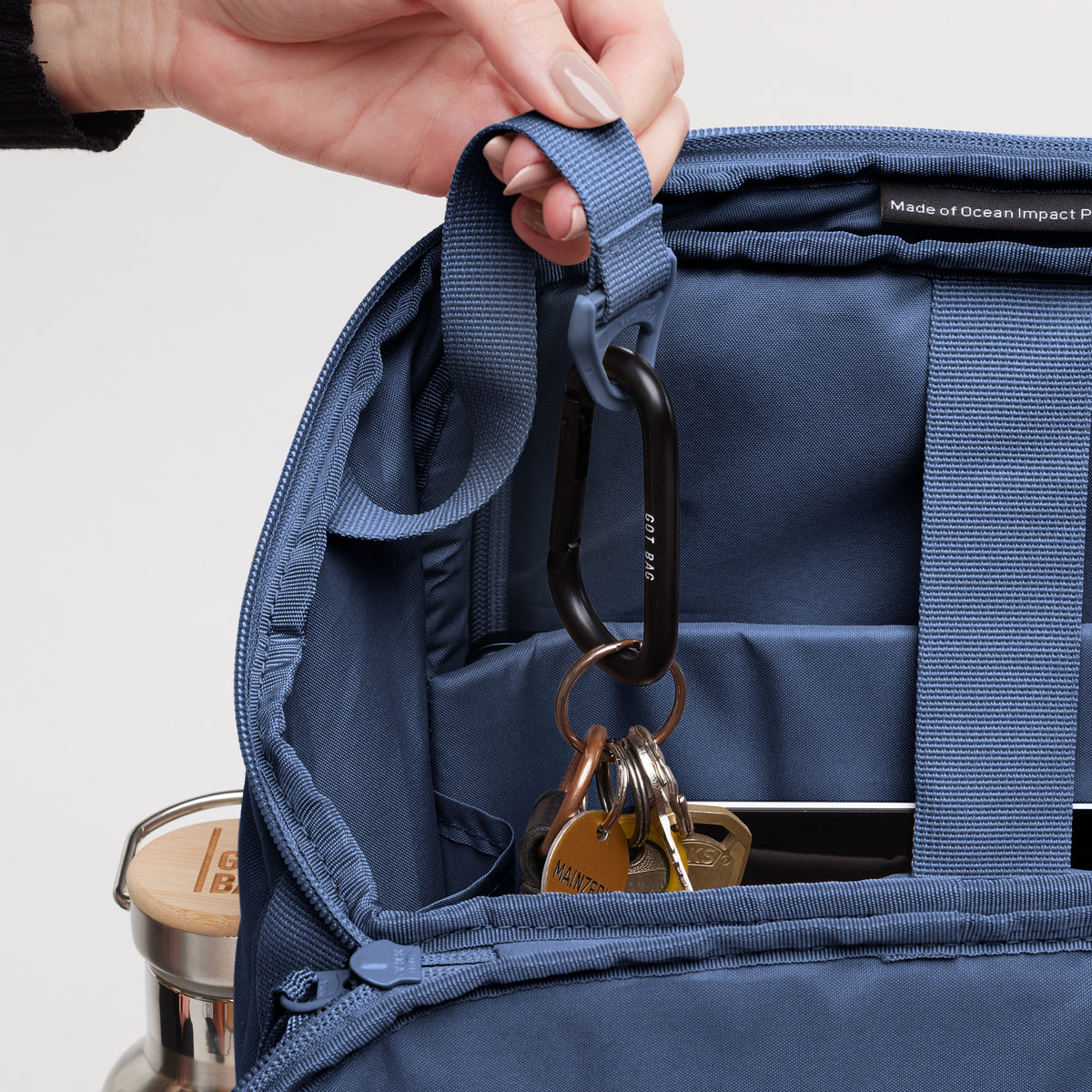 PRO PACK Rucksack. Detailaufnahme des geöffneten Innenraums mit weiblicher Hand, die einen Riemen hält, Schlüssel sichtbar.