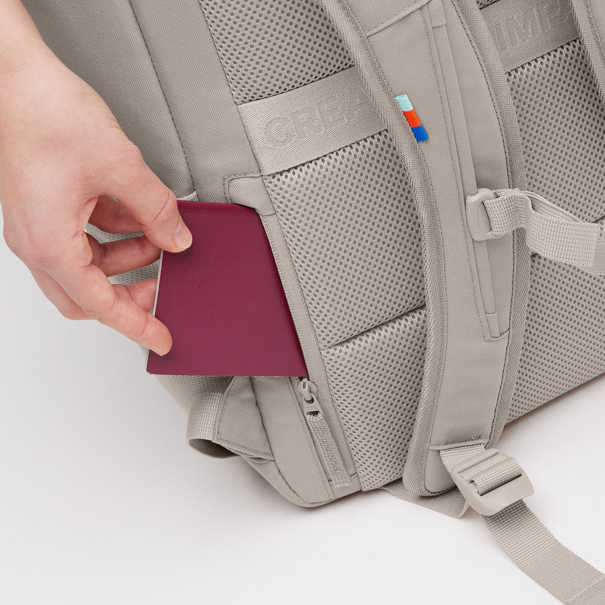 PRO PACK Rucksack in scallop (helles Beige), eine Hand steckt einen roten Reisepass in eine Seitentasche.