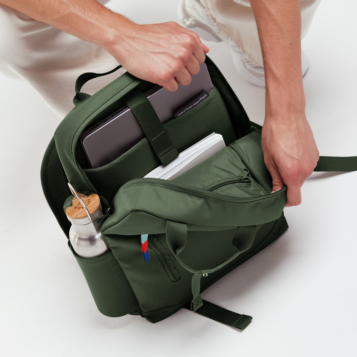 DAYPACK 2.0 Rucksack in algae (Dunkelgrün mit Graustich), von einem Mann geöffnet, zeigt Laptop, Bücher und Flasche.