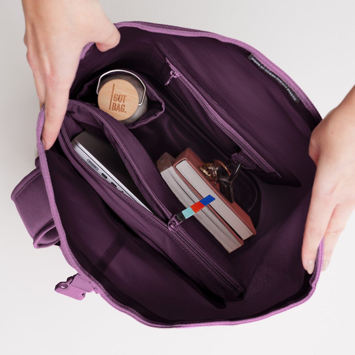 ROLLTOP 2.0 Rucksack in favia (warmes Dunkellila / Pflaumenfarben), Hände öffnen ihn und zeigen das Innere mit Fächern.