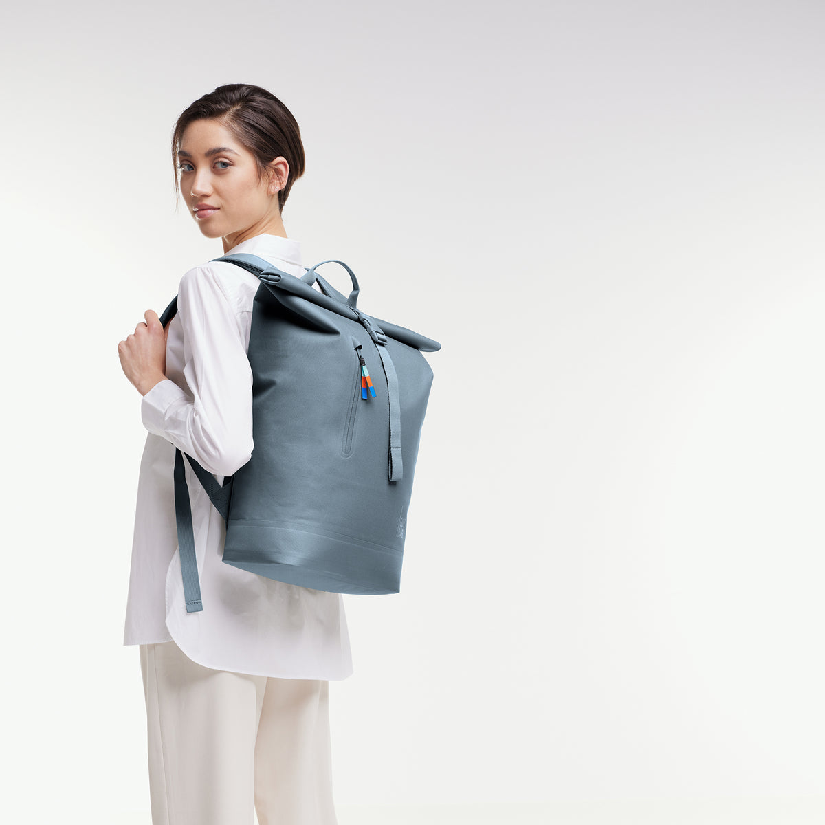 ROLLTOP LITE Rucksack in marlin (grau-blau) von einer Frau als Rucksack auf dem Rücken getragen.