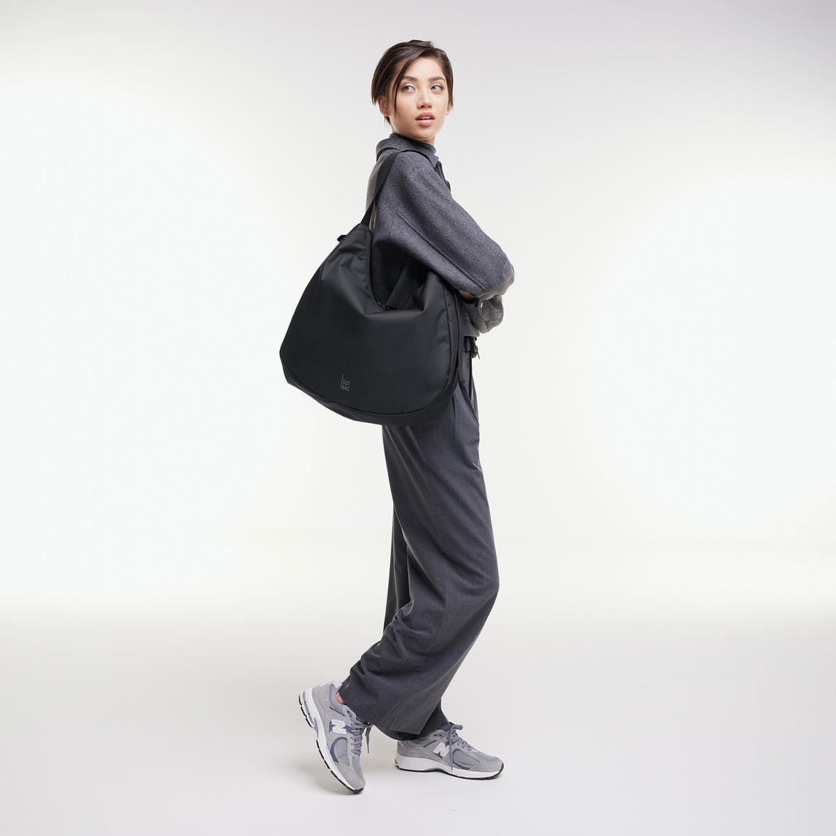 CURVED BAG Tasche in black (Schwarz) von einer Frau über der Schulter getragen.