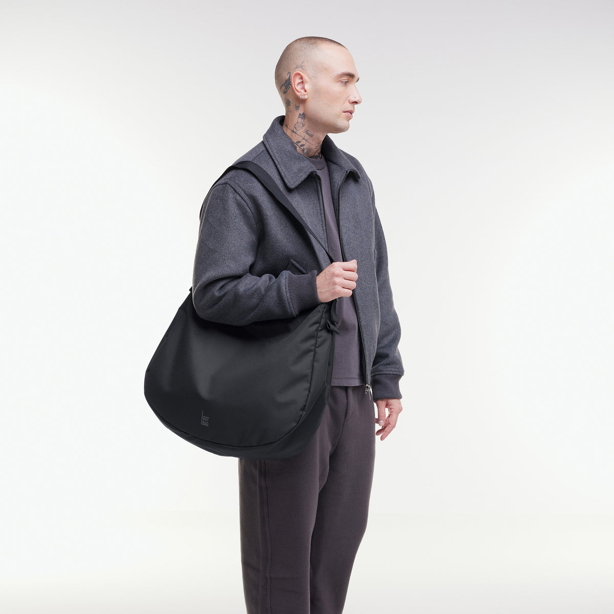 CURVED BAG Tasche in black (Schwarz) von einem Mann über der Schulter getragen.